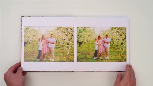 White background leaf through photobook from family photo shoot in spring garden — Stockvideo