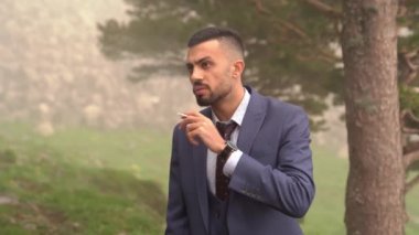Sakallı bir adam ağaçların orada sigara içiyor.. 