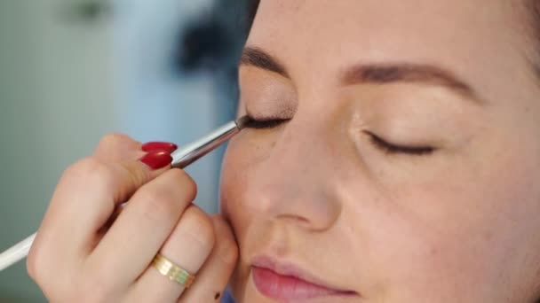 Las mujeres hacen maquillaje, pintan los párpados en los ojos con un cepillo de maquillaje. — Vídeo de stock