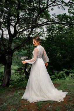 Beyaz elbiseli bir gelin dağlardaki ağaçlarda duruyor.