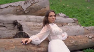 Gelin beyaz gelinlik içinde, bir tarlada, kütüklerin yanında..