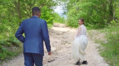Neşeli ve mutlu yeni evliler ağaçların arasında bir dağ yolunda yürüyor..
