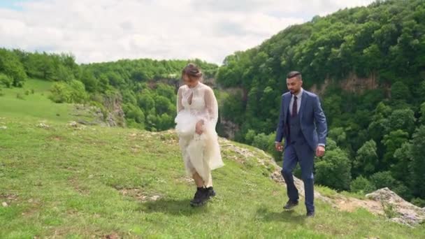 Alegres y felices recién casados caminan en un claro en las montañas — Vídeo de stock