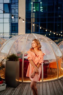 Çatı katındaki kafede pembe elbiseli çekici bir kadının portresi.