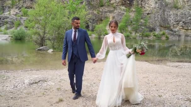 Amantes recién casados en la orilla de un lago de montaña. sesión de fotos de boda en la naturaleza — Vídeo de stock
