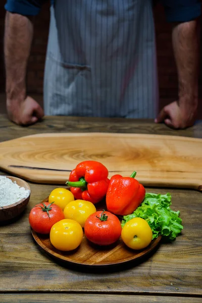 Tomates amarelos e vermelhos, alface e pimentão com gotas de água. homem de avental. — Fotografia de Stock