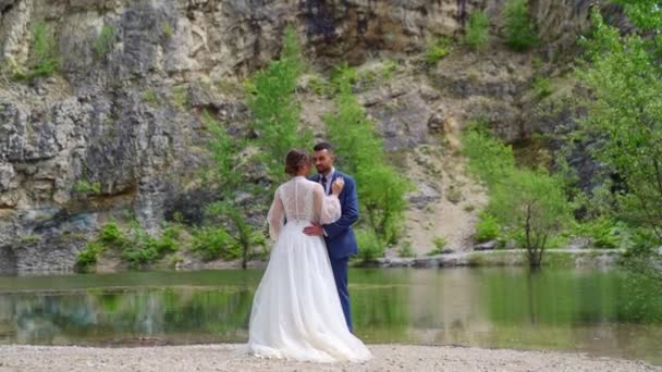 Älskade nygifta på stranden av en fjällsjö. bröllop fotografering i naturen — Stockvideo