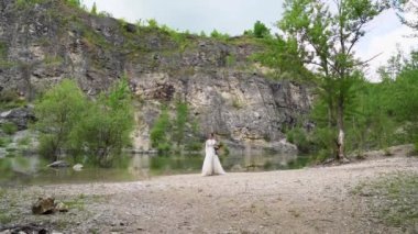 Beyaz elbiseli gelin bir dağ gölünün kıyısında yürüyor..