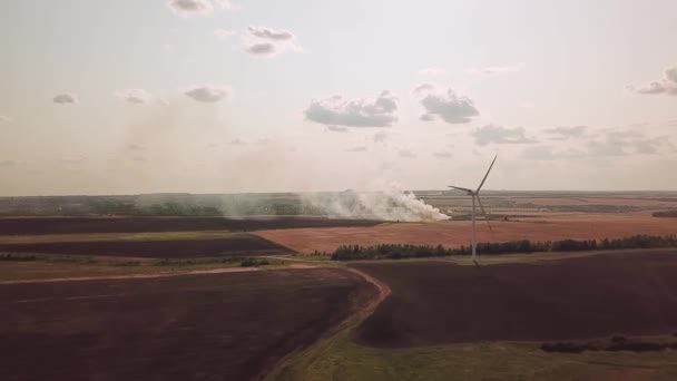 Větrné farmy na poli a hořící bohatství. ekologické protiklady. — Stock video