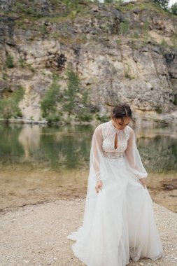 Beyaz elbiseli güzel gelin bir dağ gölünün kıyısında duruyor..