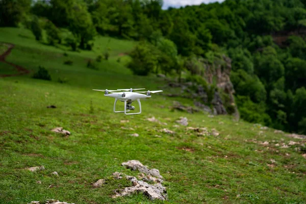 Um drone branco voa sobre as montanhas e filma um vídeo. — Fotografia de Stock