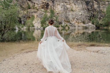 Arkadan bak. Beyaz elbiseli gelin bir dağ gölünün kıyısında duruyor..