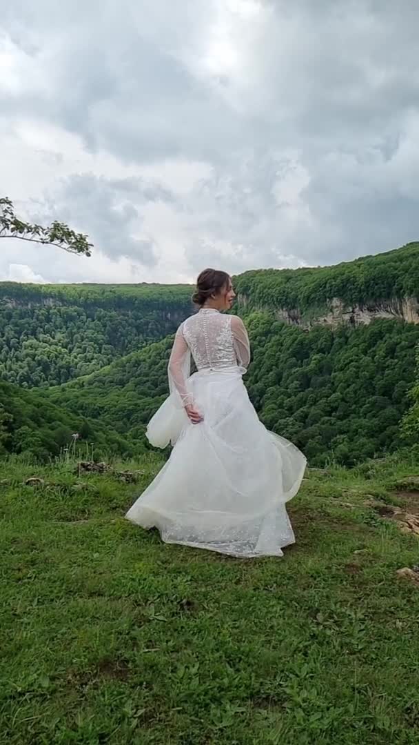 Vídeo vertical. sesión de fotos de boda en las montañas. novia girando en el prado. — Vídeos de Stock