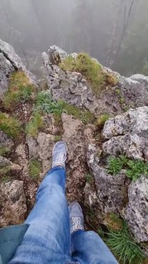 dikey video. Erkek ayağı uçurum boyunca yürür. Sisli orman manzarası.