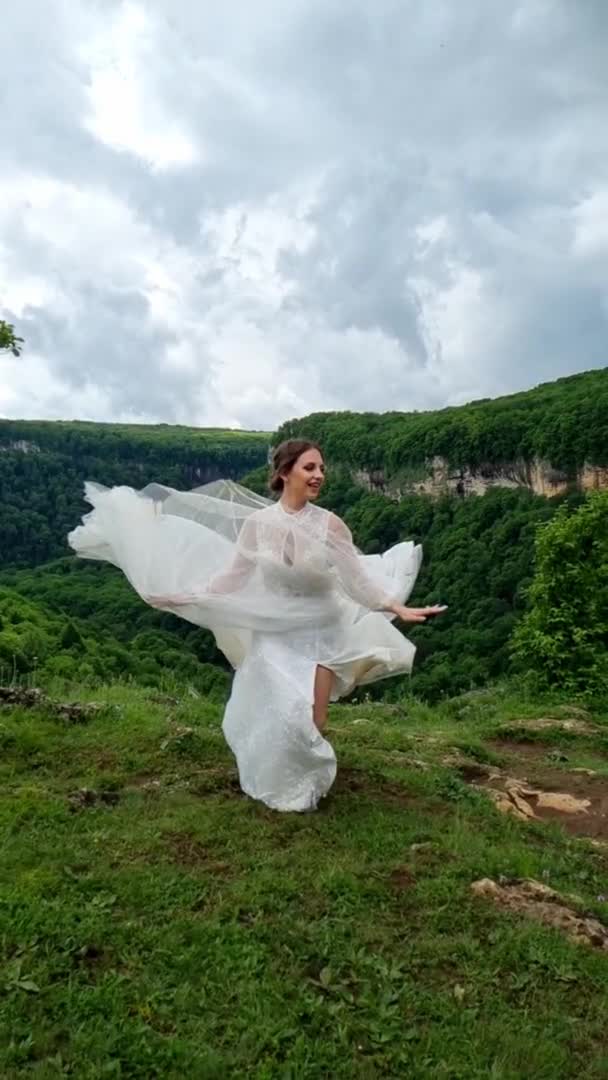 Вертикальное видео. свадебная фотосессия в горах. невеста прыгает по лугу. — стоковое видео