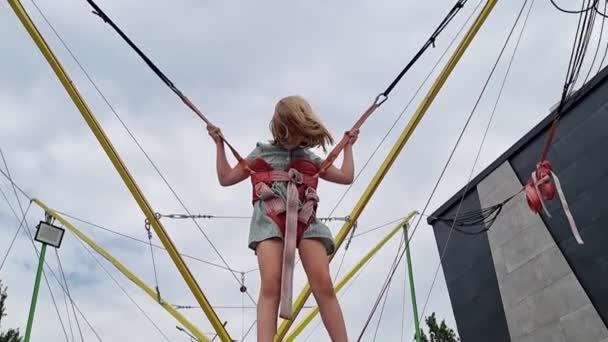Dziewczynka skacze na trampolinie na bungee. rozrywka dla dzieci w parku. — Wideo stockowe