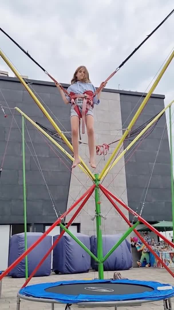 Dikey video. Genç bir kız bungee trambolinde zıplıyor. parkta eğlence. — Stok video