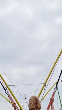 dikey video. Küçük kız bungee trambolinde zıplıyor. parkta eğlence