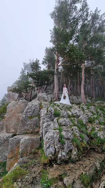 A noiva com um buquê de flores está em uma rocha na floresta de montanha. — Fotografia de Stock