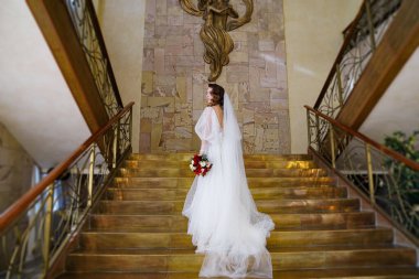 Uzun bukleli bir gelin portresi, altın merdivenlerde zarif bir elbise içinde.