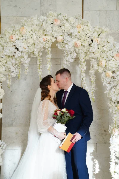 신랑 과 신부가 결혼 증명서가 들어 있는 꽃들의 아치 안에서 키스를 한다. — 스톡 사진