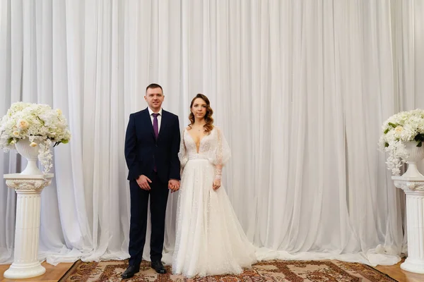 Gyönyörű és boldog menyasszony és vőlegény ellen a háttérben a fehér függöny — Stock Fotó
