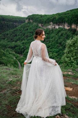 Arkadan bak. Dağlarda poz veren gelinlikli bir kadın. Gelin kıyafetleri