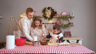 Çocuğun kendisi de yumurta kırmaya çalışıyor. Yeni yıl mutfağında mutlu ve güzel bir aile
