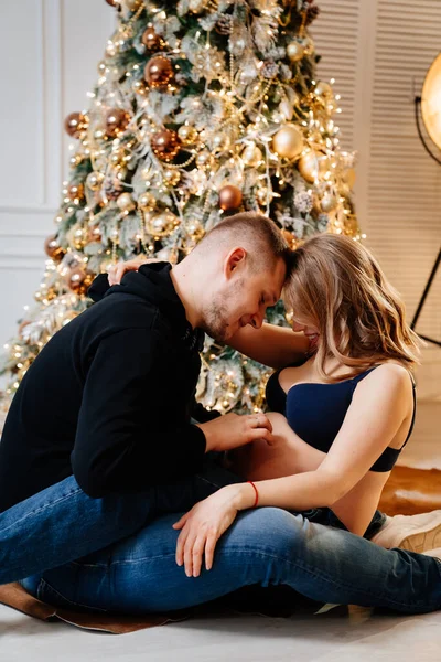 Homem feliz e mulher grávida sentado no chão pela árvore de Natal. — Fotografia de Stock