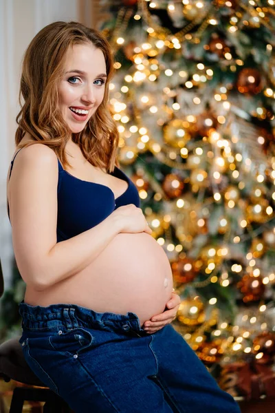 クリスマスツリーの近くに裸のおなかを持つ魅力的な妊婦 — ストック写真