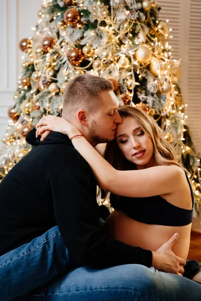 Homem feliz e mulher grávida sentado no chão pela árvore de Natal. — Fotografia de Stock