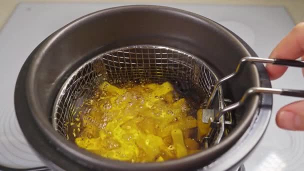 A basket of potatoes is lowered into the deep fryer. cooking french fries — Stock Video