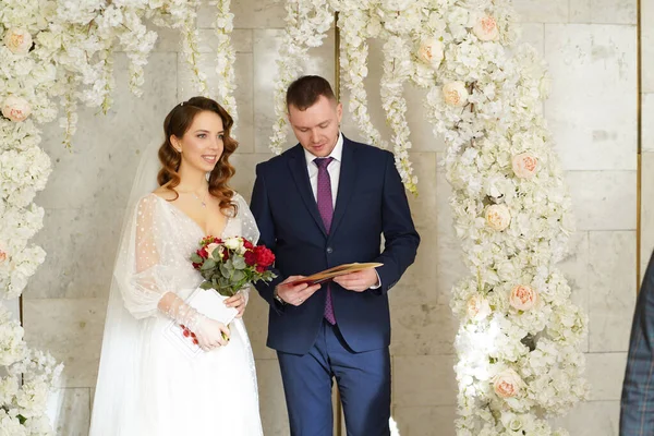 Braut und Bräutigam in einem Blumenbogen bei einer Zeremonie mit Trauschein. — Stockfoto