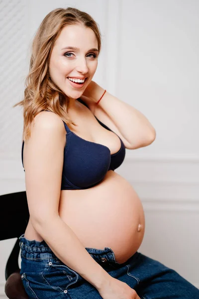 Uma mulher grávida atraente com uma barriga nua senta-se em uma cadeira. — Fotografia de Stock