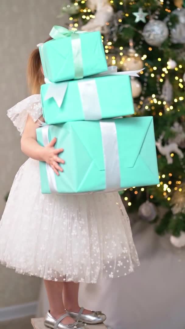 Bambina tiene una torre di scatole regalo sotto l'albero di Natale e cade — Video Stock