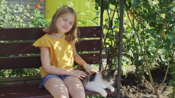 Klein meisje streelt verdwaalde kat zitten op een bank met mooie landschapsarchitectuur — Stockvideo