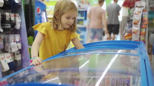 Engraçado bonito menina no supermercado com carrinho de compras escolhe o que comprar — Vídeo de Stock