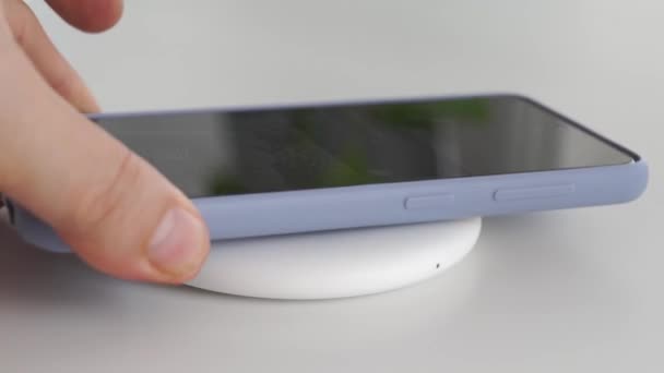 Smarttelefonen placeras på en vit rund trådlös laddare. — Stockvideo