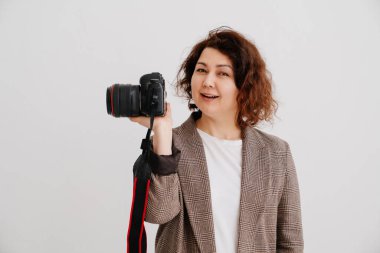 Dişli ceketli çekici esmer kadın beyaz arka planda ve kameralı.