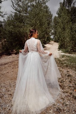 Arkadan bak. Gelinlikli kadın ağaçlar arasında dağ yolunda yürüyor..