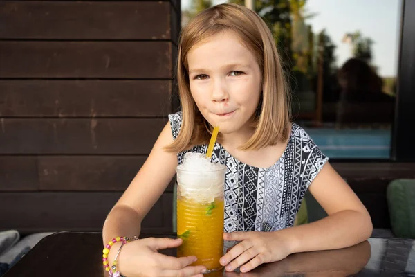 Funny little girl drinks through cocktail tube tropical cocktail. family cafe, summer veranda