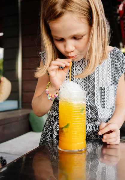 Funny little girl drinks through cocktail tube tropical cocktail. café familial, véranda d'été — Photo