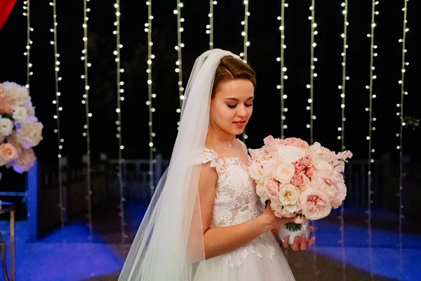 Mariée avec bouquet de fleurs dans le parc de nuit sur fond de guirlande. — Photo