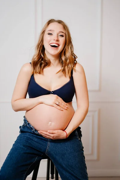 Een aantrekkelijke zwangere vrouw met een kale buik zit op een stoel. — Stockfoto