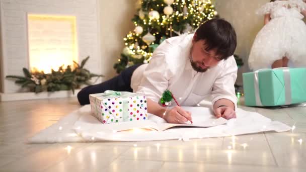 Papà e figlioletta scrivono una lettera a Babbo Natale sotto l'albero di Natale. — Video Stock