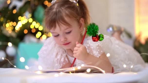 Holčička napíše dopis Santovi pod vánoční stromeček. — Stock video