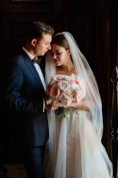 Glückliche Braut und Bräutigam mit einem Strauß in einem dunklen Interieur. — Stockfoto