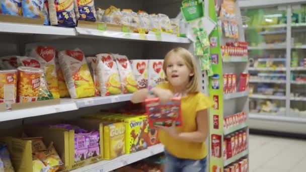 Lucu gadis lucu di supermarket dengan keranjang belanja memilih apa yang harus membeli — Stok Video