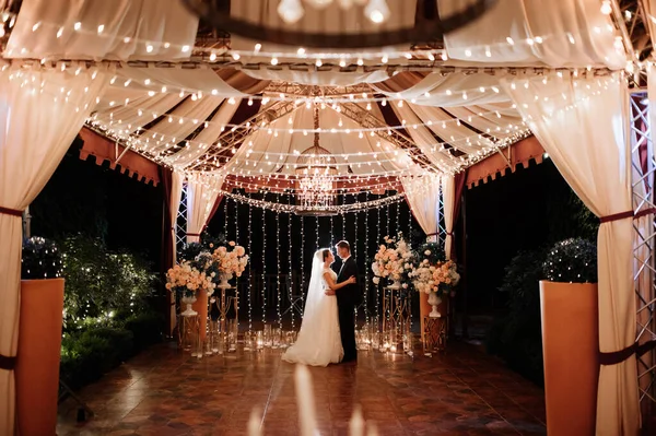 De bruid en bruidegom op de nachtstraat tussen de bloemenslingers — Stockfoto