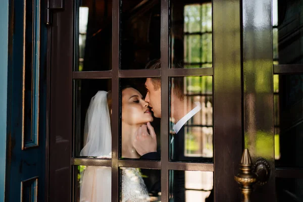 Noiva e noivo através da porta de vidro. casamento bonito e feliz. — Fotografia de Stock